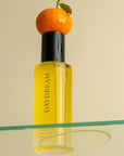 Orchid + Ash Daydream All-Natural Body Oil - Orange + Neroli - product shown with orange and oil dripping onto glass surface