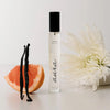 Lifestyle shot of Orchid + Ash Aura Travel Spray - Grapefruit + Tonka Bean with vanilla bean pods, grapefruit slice and white flower in the background