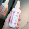 R+Co Candy Stripe Protect + Prep Detangling Spray - model holding product in front of mirror