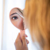 Rye Beauty Brow Milk - model shown using brow brush holding a mirror