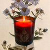The Quiet Botanist In The Weeds Scented Candle - lit candle shown in front of flowers