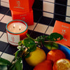 ROEN Candles La Condesa Scented Candle - product shown lit next to bowl of fruit and packaging