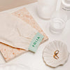 Folia Body Exfoliating Tan Removal Mitt - product shown on sink next to glasses, stone slab, and earrings