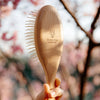 Snow Fox Skincare Gua Sha Hair & Scalp Brush: Premium Wooden Edition - close up of model holding product showing back side of brush with Snow Fox Skincare logo