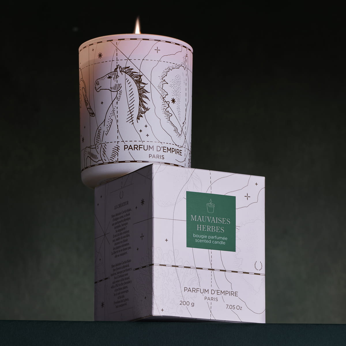 Lifestyle shot of Parfum d'Empire Mauvaises Herbes Scented Candle (200 g) shownn lit sitting on box