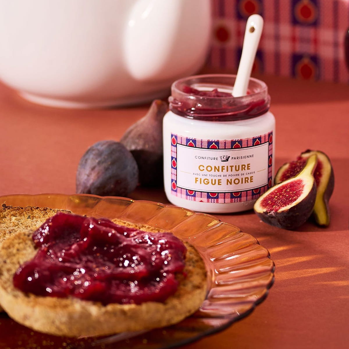Lifestyle shot of open jar of Confiture Parisienne Black Fig & Blackcurrant Pepper (100 g) with figs next to jar and jam spread on toast
