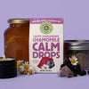 Life style shot of Chamomile Life Happy Huckleberry Chamomile Calm Drops (85 g) with chamomile flowers and Calm Drops in the background
