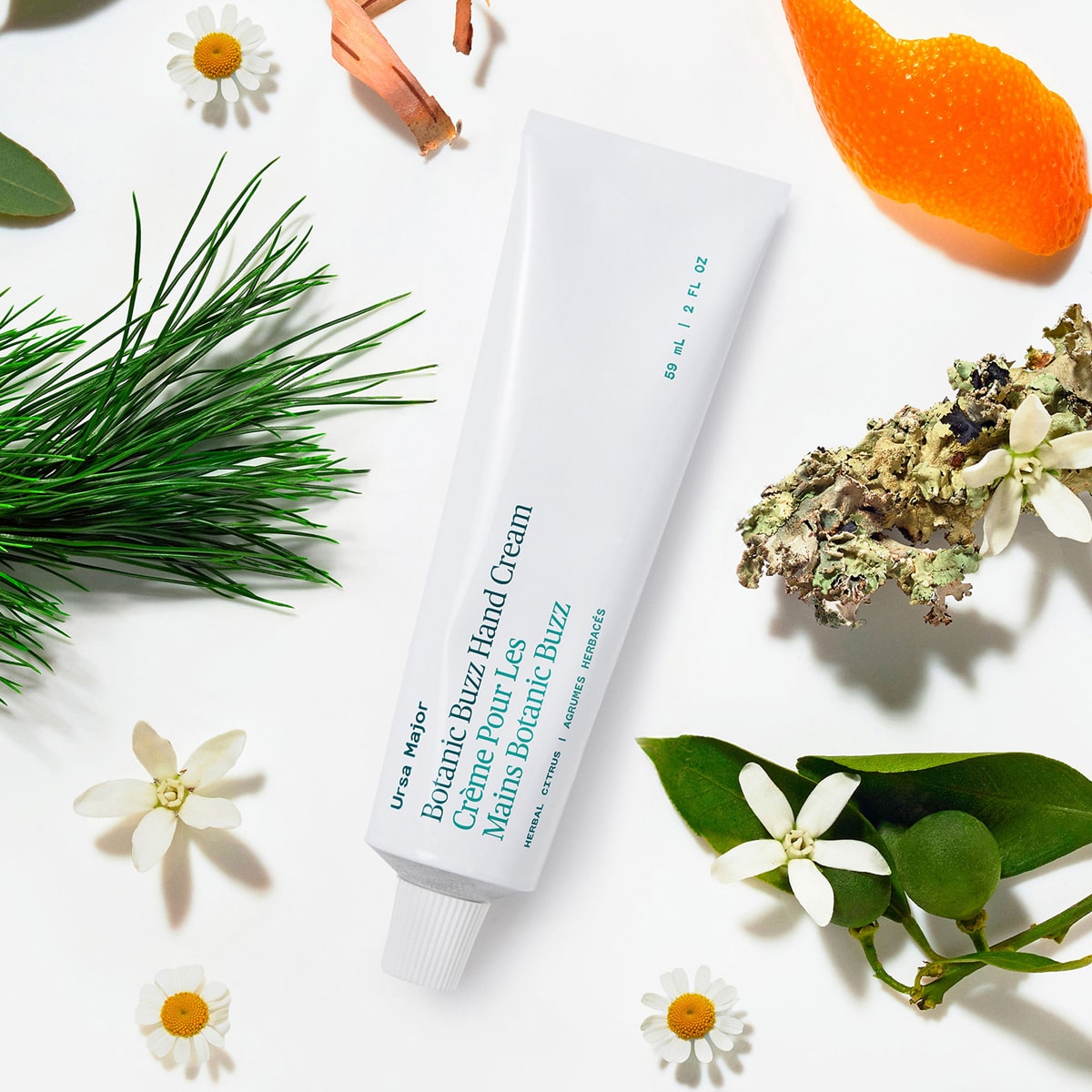 Ursa Major Botanic Buzz Hand Cream (2 oz) tube surrounded by greenery and flowers on a white background