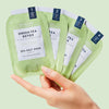 Hand holding VOESH New York Pedi In A Box - Green Tea Detox (4 pcs - individual packets) against a light green background