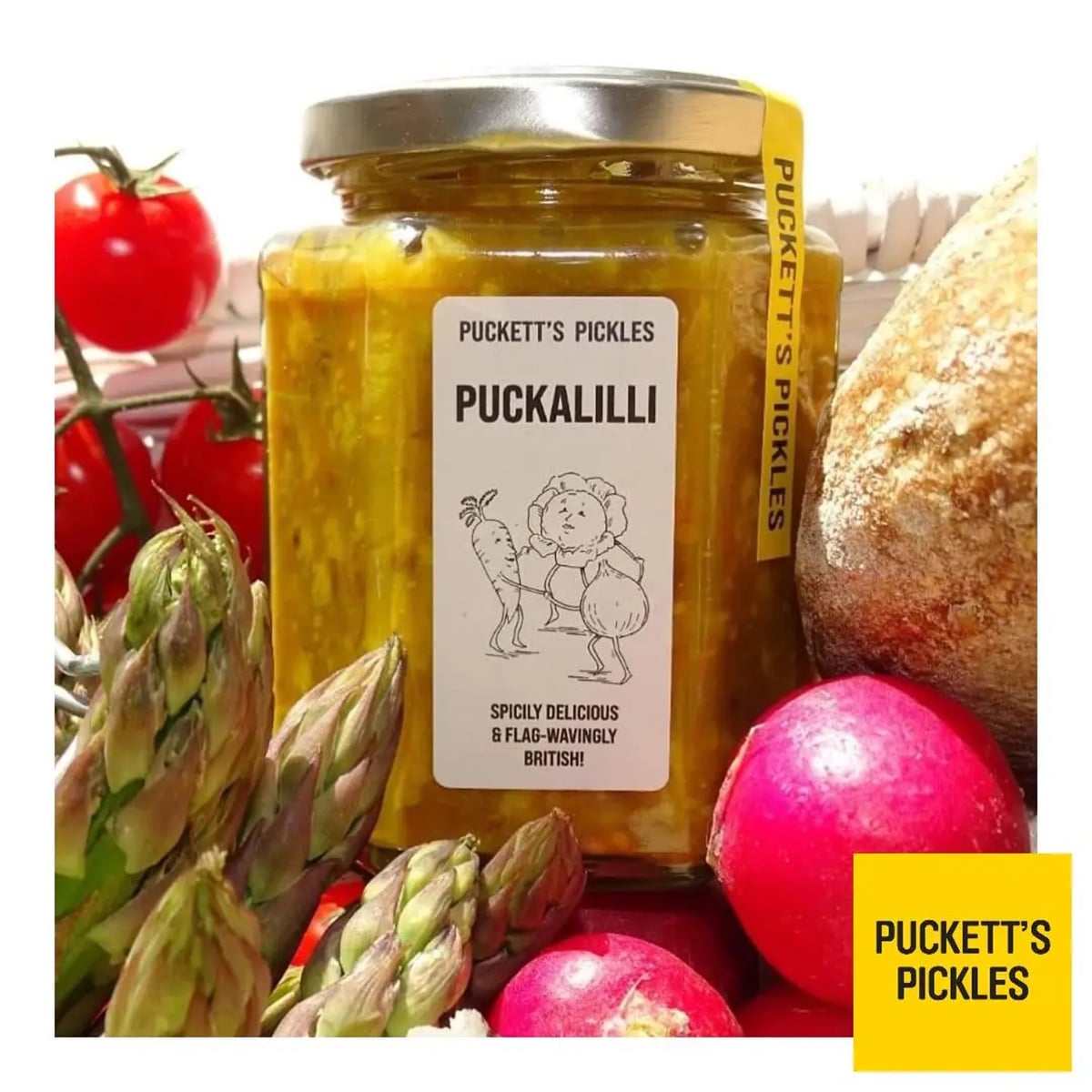 Puckett’s Pickles Puckalilli (340 g) bottle shown surrounded by asparagus, cherry tomatoes, radishes and bread crust