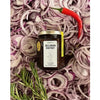 Puckett’s Pickles Red Onion Chutney (226 g) bottle shown on a pile of red onions with a red chili pepper and rosemary sprig on the side