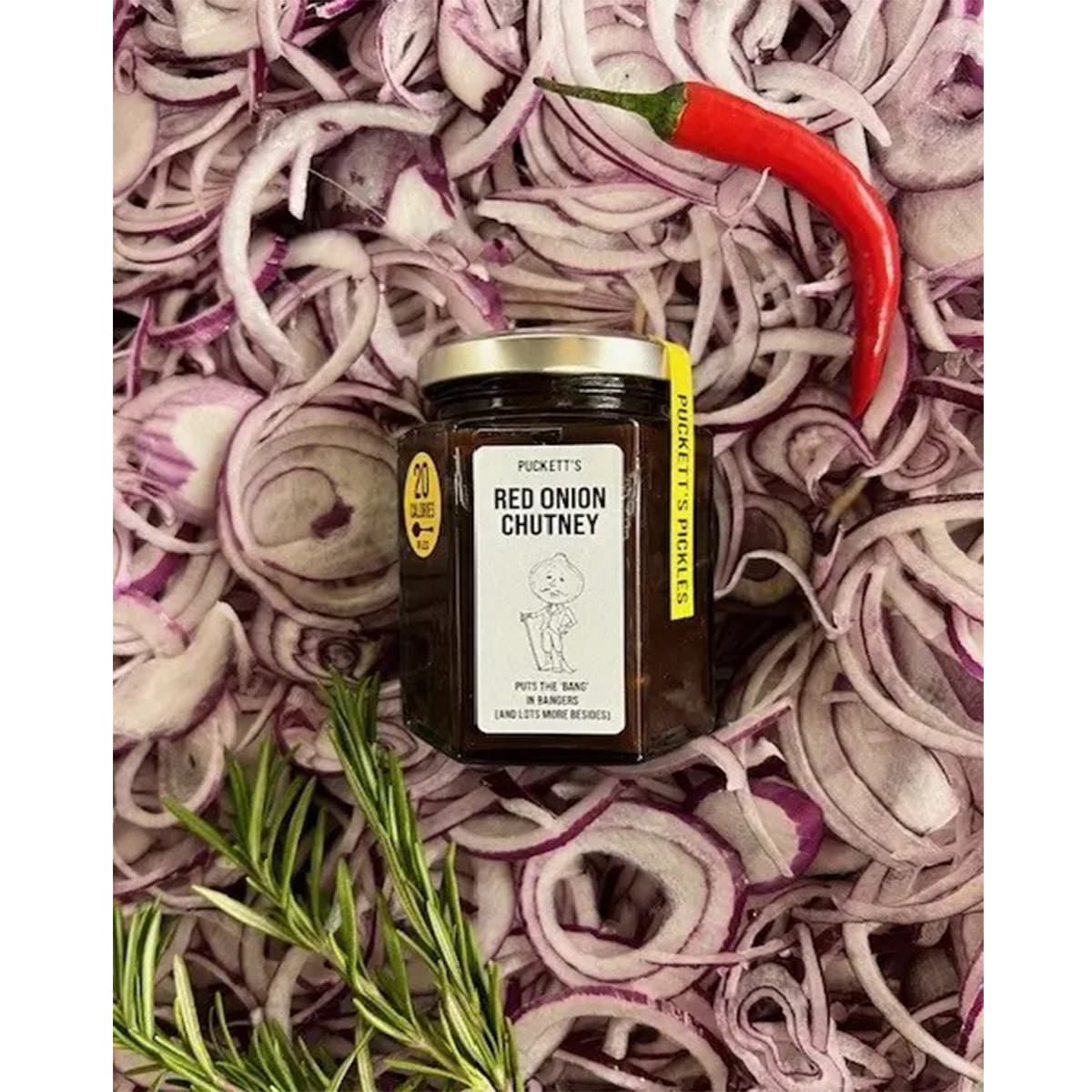 Puckett’s Pickles Red Onion Chutney (226 g) bottle shown on a pile of red onions with a red chili pepper and rosemary sprig on the side