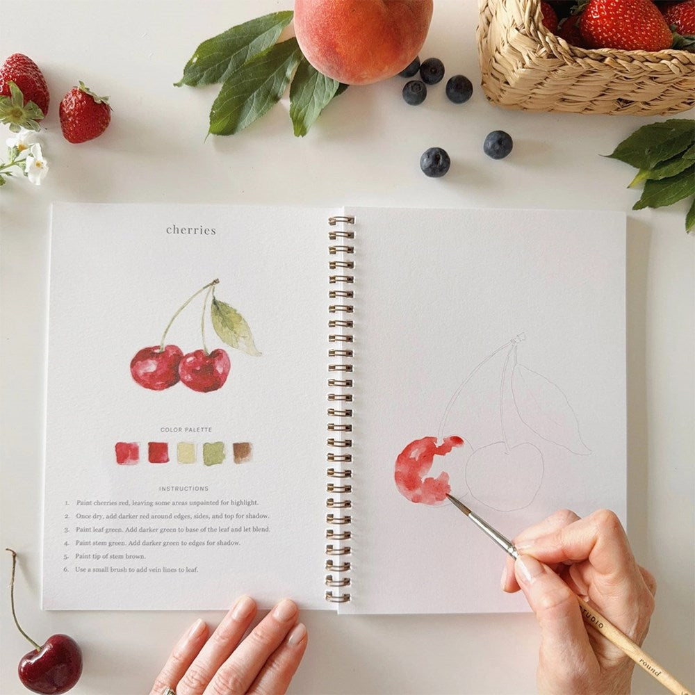 Emily Lex Studio Fruit Watercolor Workbook - product shown open with paint brush and hands
