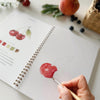 Emily Lex Studio Fruit Watercolor Workbook - product shown open with paint brush and hands