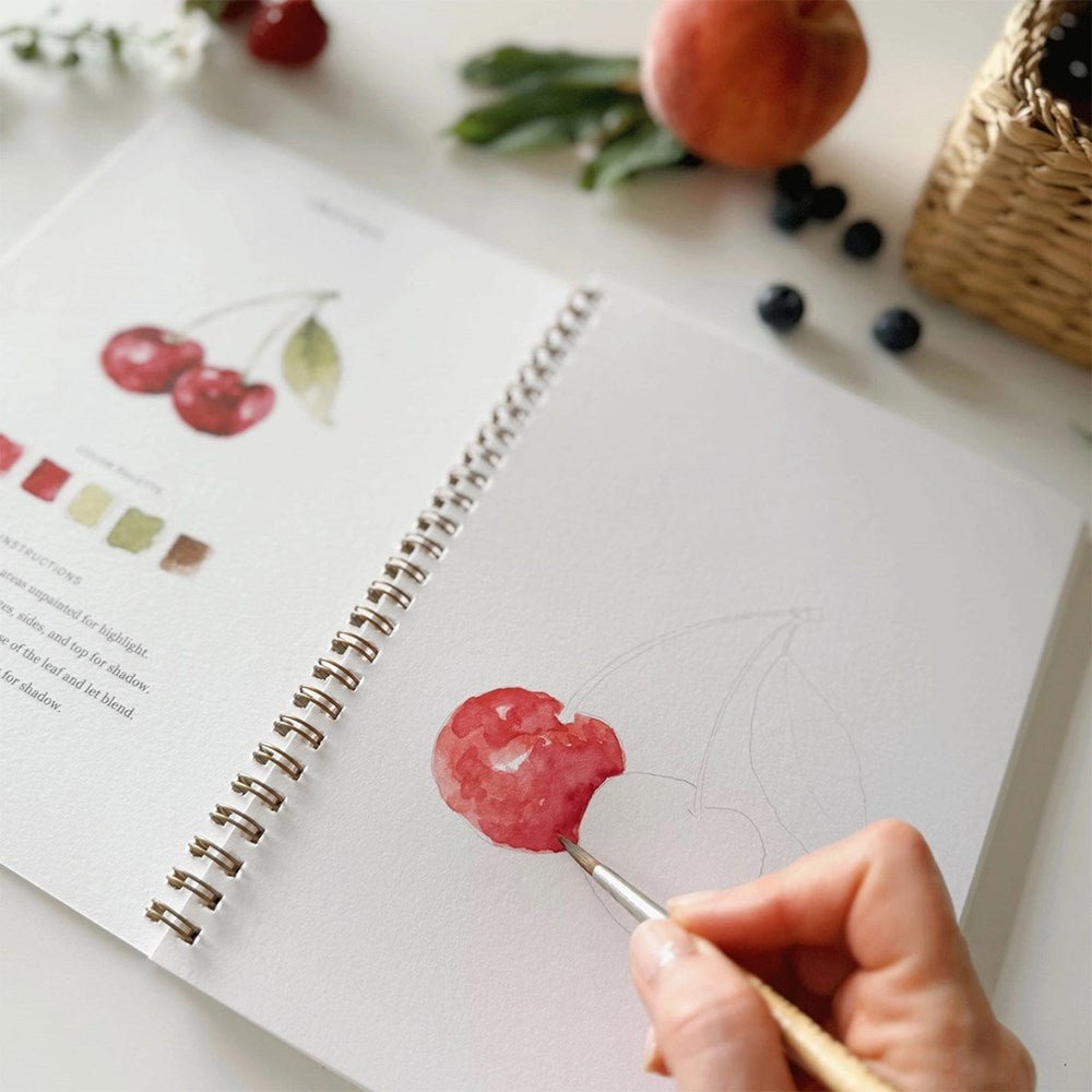 Emily Lex Studio Fruit Watercolor Workbook - product shown open with paint brush and hands