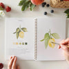 Emily Lex Studio Fruit Watercolor Workbook - product shown open with paint brush and hands
