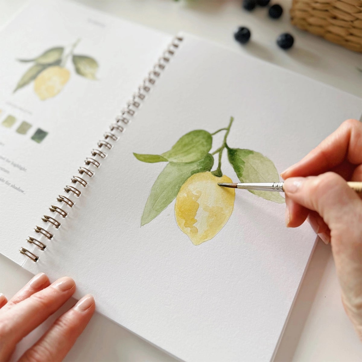 Emily Lex Studio Fruit Watercolor Workbook - product shown open with paint brush and hands