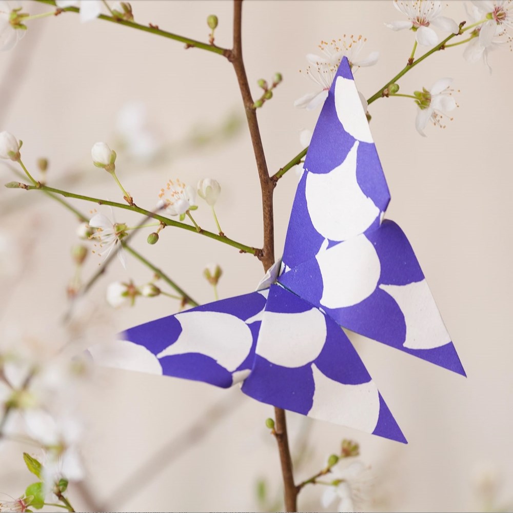 Cambridge Imprint Origami Cloud of Butterflies Kit (36 pc) hanging from a branch with flowers.
