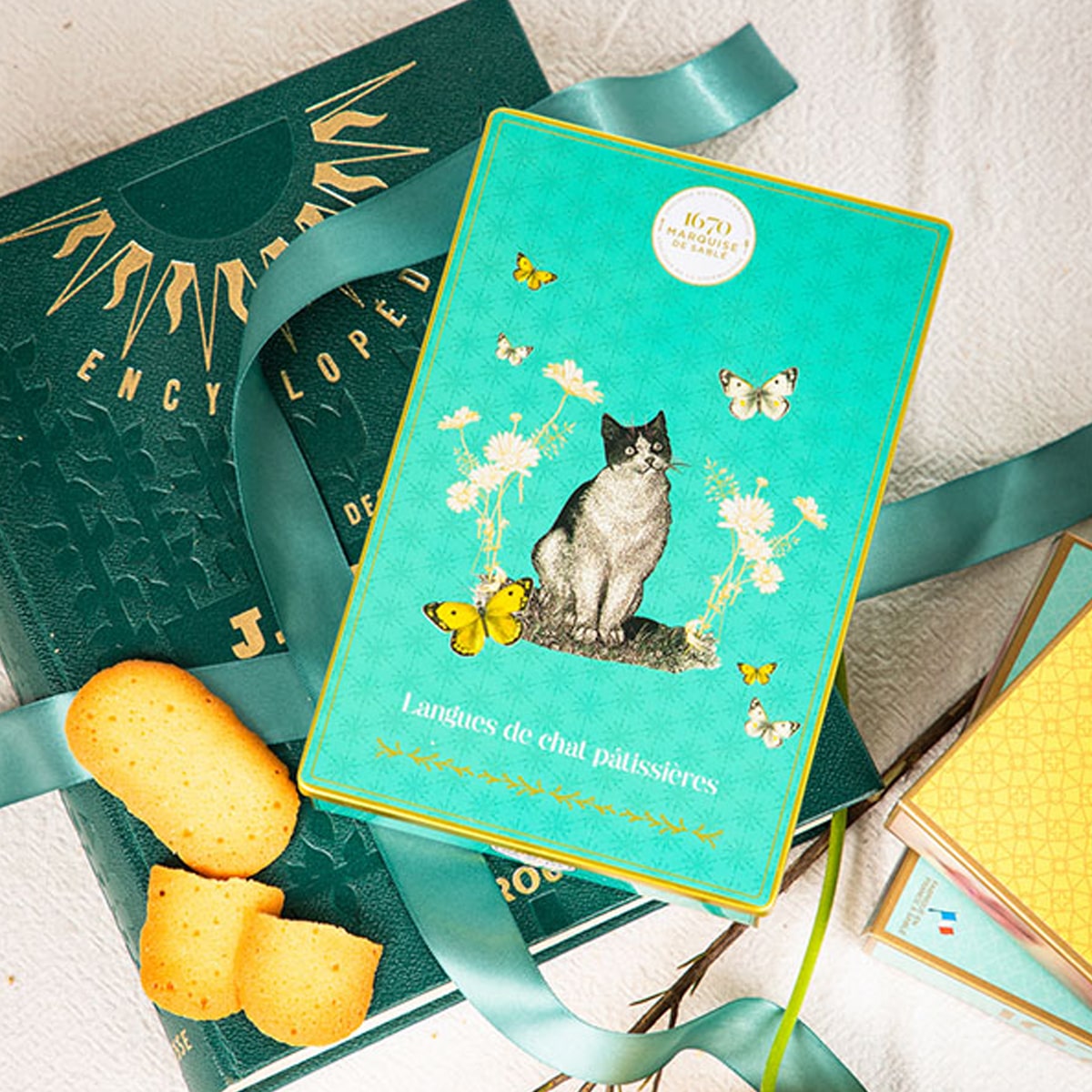 La Sablesienne Pastry Cat Langues Box (160 g) - product shown on a book and ribbon next to cookies 