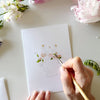 Person painting Emily Lex Studio Bouquets Paintable Notecards (8 pcs) with flowers around.