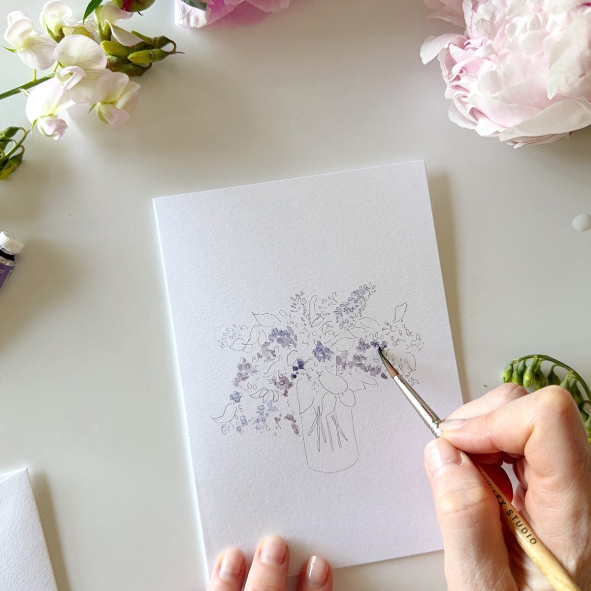 Person painting Emily Lex Studio Bouquets Paintable Notecards (8 pcs) with flowers and art supplies around