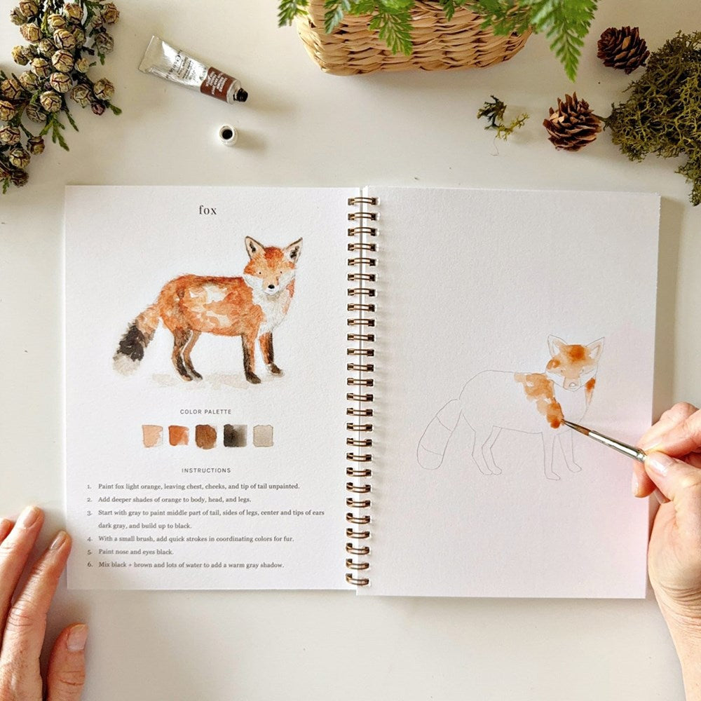 Emily Lex Studio Woodland Watercolor Workbook (1 pc) being painted by a hand.