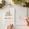 Emily Lex Studio Woodland Watercolor Workbook (1 pc) surrounded by decorative elements on a light surface.