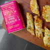 Diaspora Co. Pahadi Pink Garlic (2.11 oz) tin shown on a wooden board with cheesy bread using Pahadi Pink Garlic powder