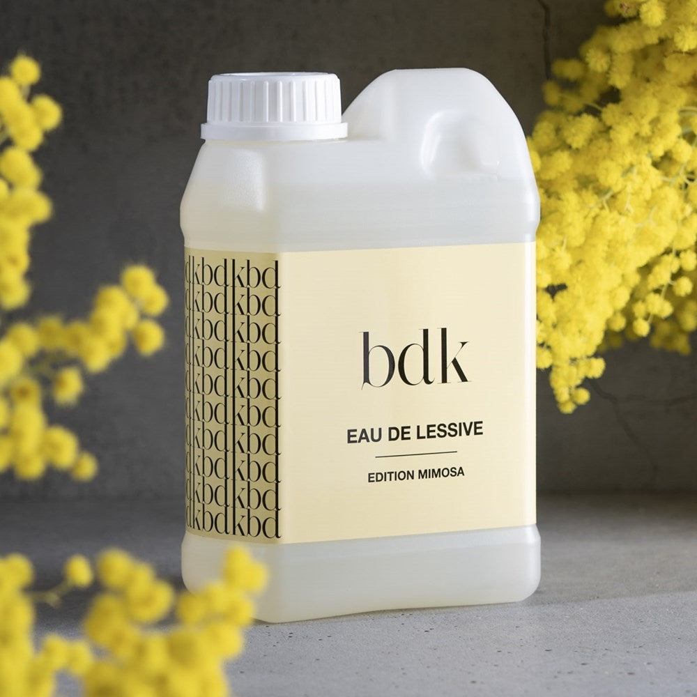 BDK Parfums Eau de Lessive Mimosa (1 liter)- product shown next to yellow flowers. 