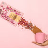 Lifestyle shot of Elements Rose Cocoa Mix Drinking Chocolate (8 oz) with rose petals and cocoa mix and pink mug in model's hand