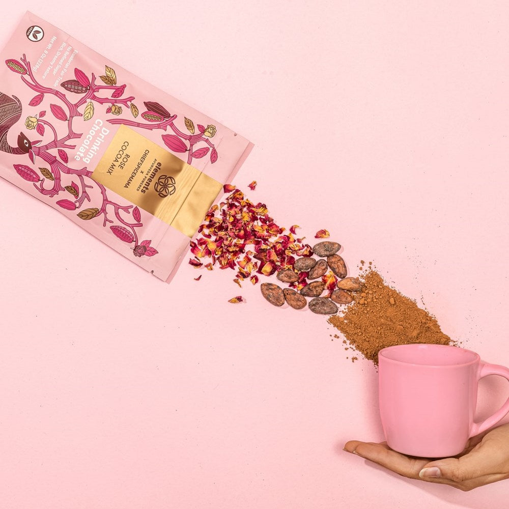 Lifestyle shot of Elements Rose Cocoa Mix Drinking Chocolate (8 oz) with rose petals and cocoa mix and pink mug in model's hand