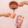 Lifestyle shot of Elements Rose Cocoa Mix Drinking Chocolate being poured into mug