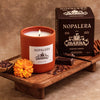 Nopalera Chocolate Ibarra Candle (8.5 oz) on a wooden tray with box and ingredients including chocolate and cinnamon.