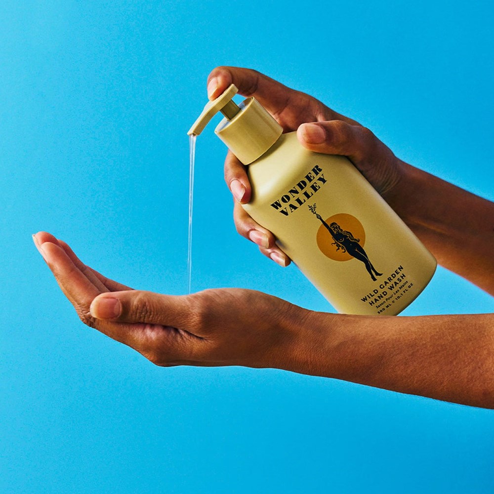 Hand holding a bottle and dispensing Wonder Valley Wild Garden Hand Wash (300 ml) and against a blue background