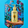 Hand holding Wonder Valley Wild Garden Hand Wash (300 ml) background with flowers.