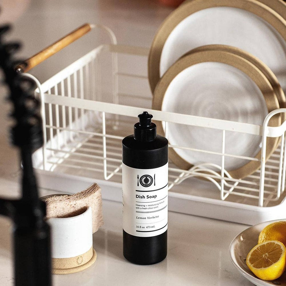 Farmhouse Pottery Potter’s Dish Soap - Lemon Verbena (16 oz) on a kitchen counter with a dish rack and plates in the background