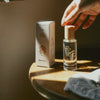 Kerzon Eau de Parfum - Bois D’Hinoki (50 ml)- product shown on wooden table with hand in top right. 