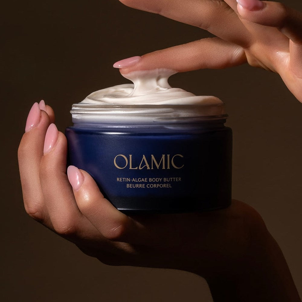 Lifestyle shot of model holding Olamic Retin-Algae Body Butter (6.7 oz) with lid off and finger dipped in body butter