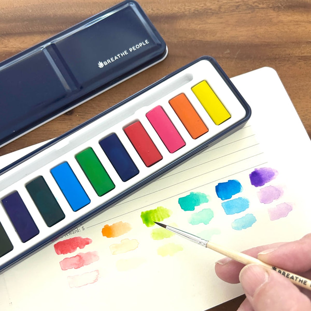 Breathe People Watercolor Paint Set with person creating colorful swatches on paper on a wood table
