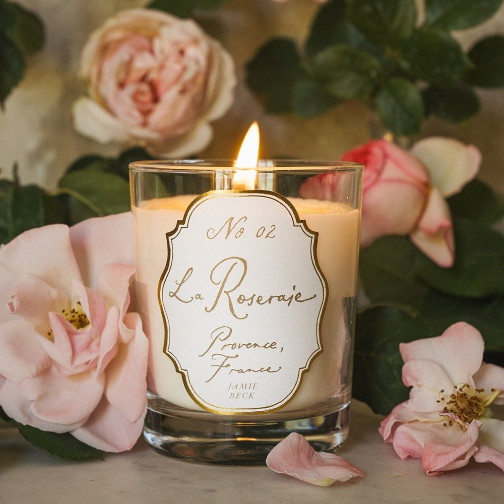 Jamie Beck La Roseraie Candle (6.34 oz) - product shown lit with roses in background. 