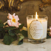 Jamie Beck La Roseraie Candle (6.34 oz) - product shown lit next to a flower in the background. 