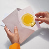 Octaevo Sun Greeting Card and Multi-use Metal Clip (1 pc) - product shown being put in an envelope. 