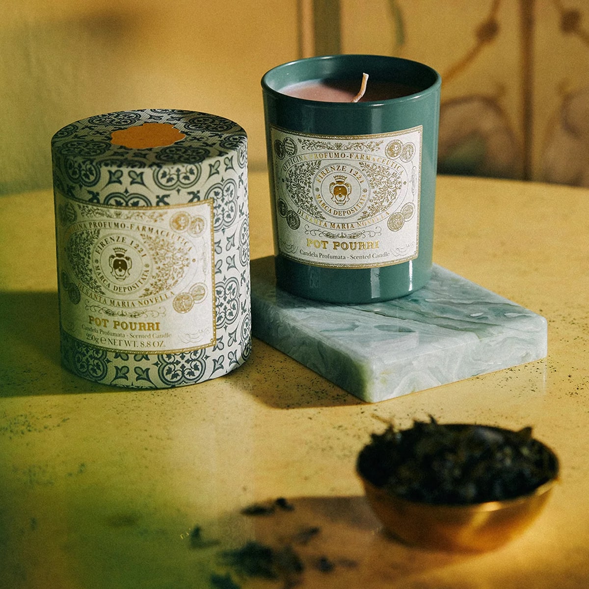 Lifestyle shot of Santa Maria Novella Pot Pourri Scented Candle (250 g)  with small gold bowl with pot pourri in the foreground