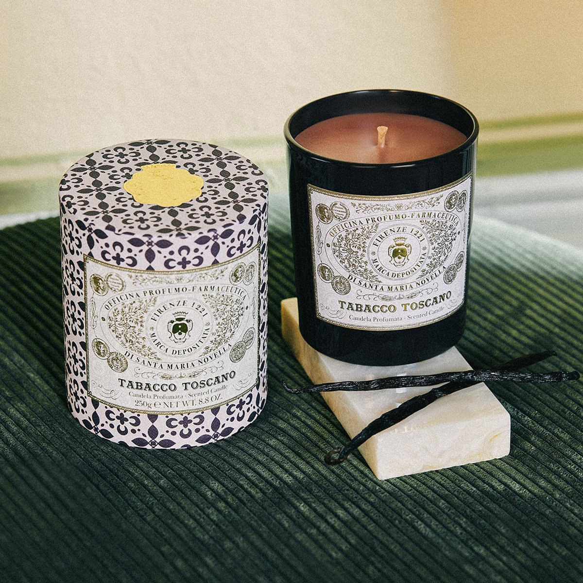Lifestyle shot of Santa Maria Novella Tabacco Toscano Scented Candle (250 g) with vanilla bean pods next to candle