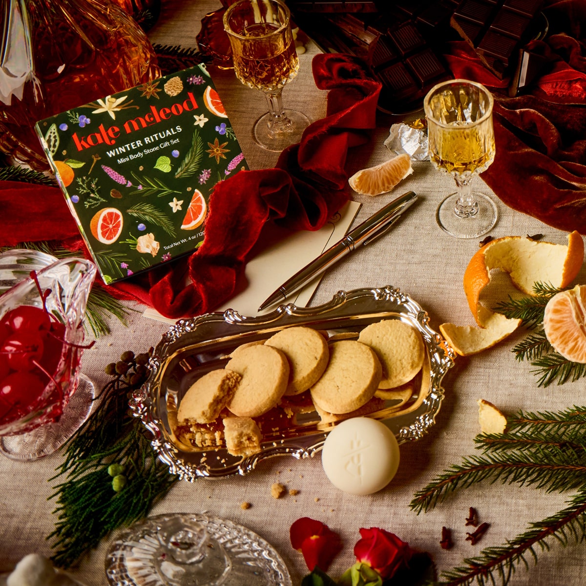 Lifestyle shot of Kate McLeod Winter Rituals Mini Body Stone Gift Set (4 pcs) - table setting with cookies, drinks, on a festive tablecloth