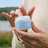 Close up of model holding open jar of Ursa Major Vital Spring Hydration Mask (1.69 oz)