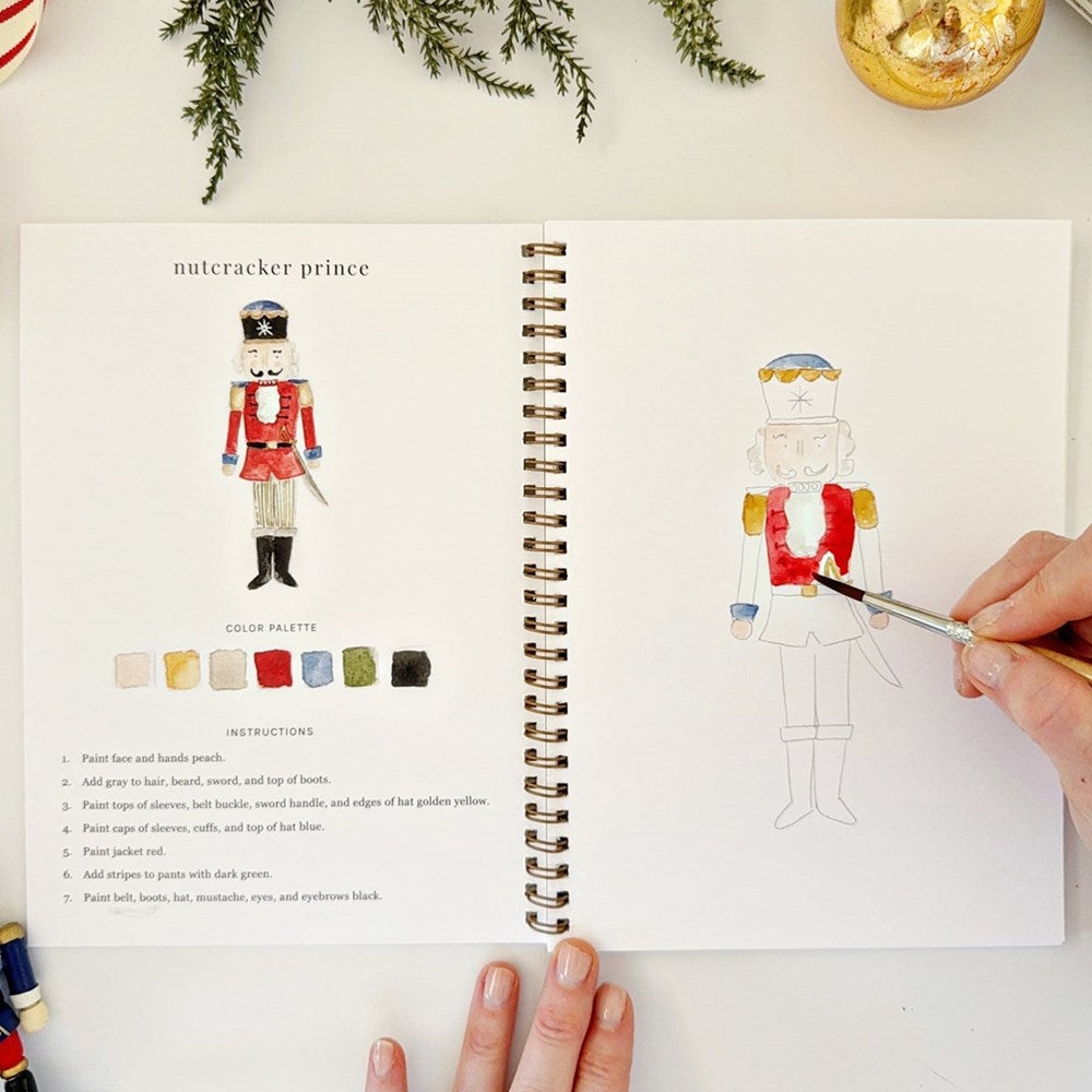 Emily Lex Studio Nutcracker Watercolor Workbook (1 pc) - page of product shown with hand and paintbrush. 