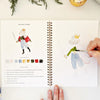 Emily Lex Studio Nutcracker Watercolor Workbook (1 pc) - page of product shown with hand and paintbrush. 