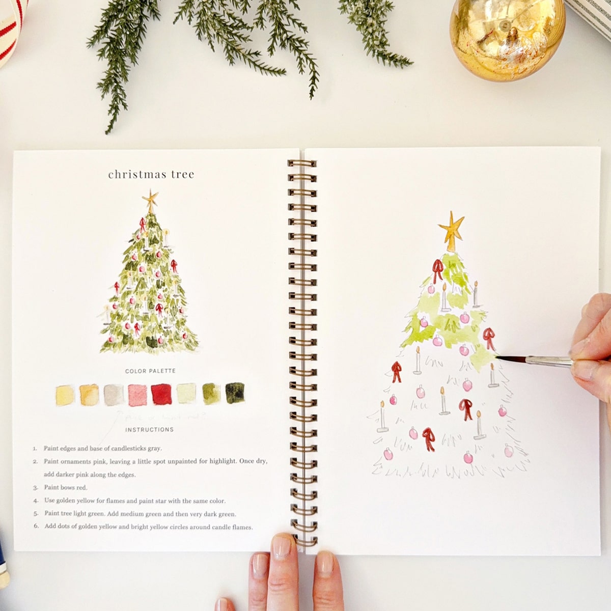 Emily Lex Studio Nutcracker Watercolor Workbook (1 pc) - page of product shown with hand and paintbrush. 