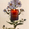 The Quiet Botanist In The Weeds Mini Candle (3 oz) - product shown in front of flowers.
